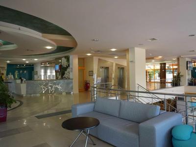 Modernes, helles Empfangsgebiet mit grauem Sofa, Rundtisch, Pflanzen und infomatischem Tresen.