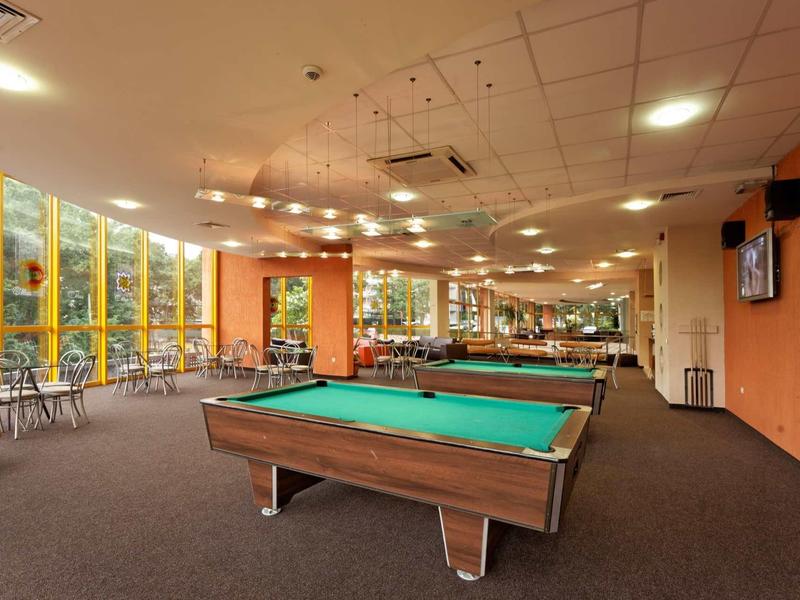 Interiér rekreačního prostoru s kulečníkovými stoly a posezením u velkých oken.