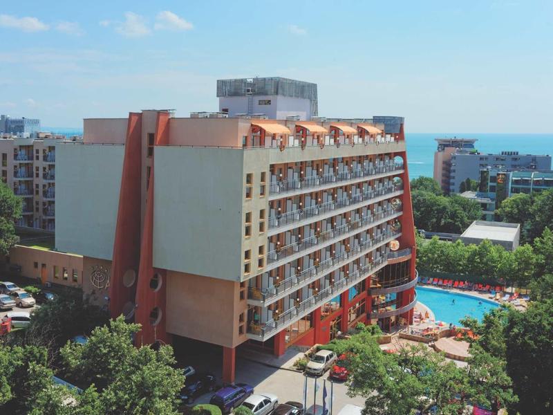 Velká hotelová budova s balkony vedle venkovního bazénu a hustou zelení.