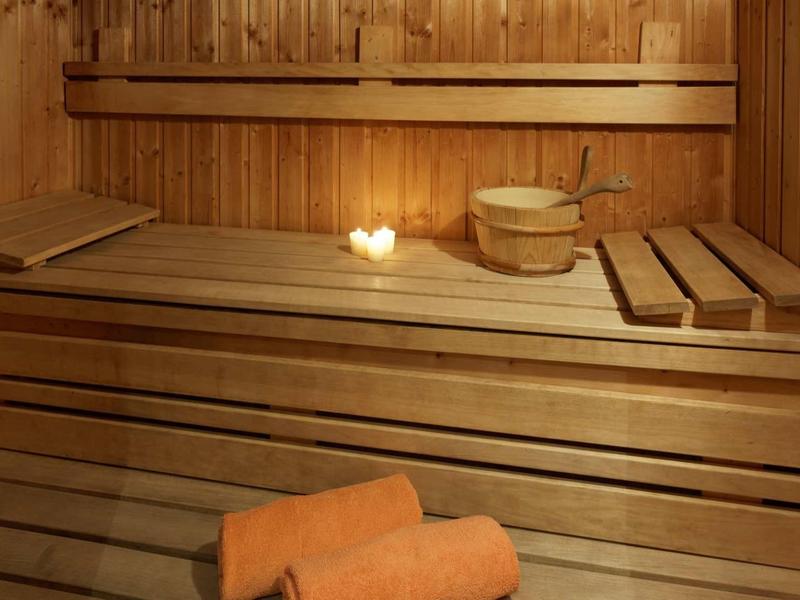 Pohodlná sauna s dřevěnými lavicemi, světlem svíčky a saunovými doplňky.