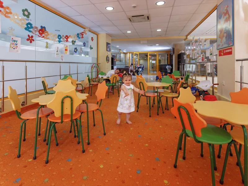 Dítě chodí barevnou hotelovou jídelnou s stoly a židlemi.