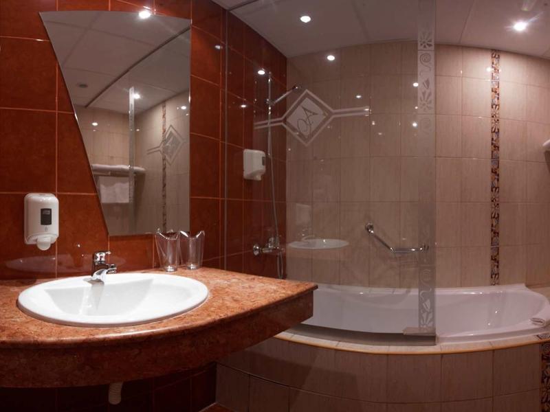 Moderní hotelová koupelna se umyvadlem, zrcadlem a vanou s paravánem na sprchu.