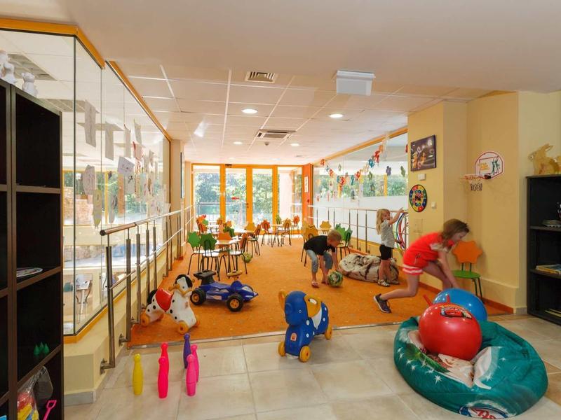 Děti si hrají v světlé, prostorné herně s barevnými hračkami.