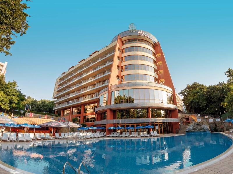 Moderní hotelová budova s bazénem a lehátky pod jasnou oblohou