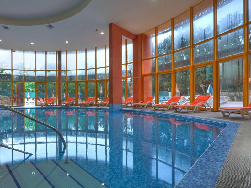 Vnitřní bazén s velkými okny a oranžovými lehátky vedle vody.