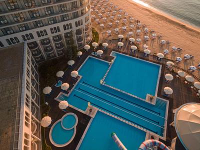 Hotelpool mit mehreren Schwimmbecken und Sonnenschirmen am Strand bei Sonnenuntergang.