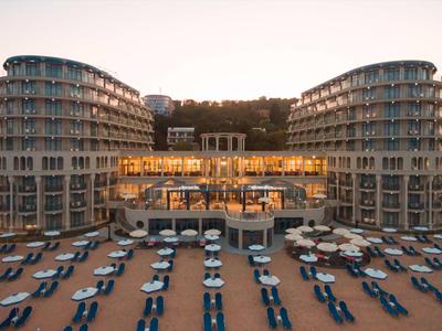 Modernes Hotel mit zwei rundlichen Türmen, Terrassen und Reihen von blauen Liegen am Strand.