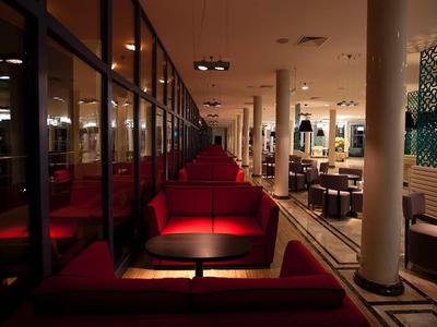 Dimmer Innenraum eines Restaurants mit roten Sitzbänken, Tischen und Glaswänden links.