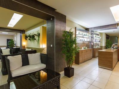 Moderne, helle Empfangshalle mit Sitzbereich, Pflanzen und Holztheke, weiße Kissen und Deckenlicht.