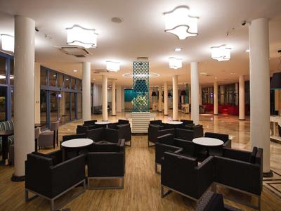 Moderner Aufenthaltsraum mit schwarzen Sitzgruppen, runden weißen Tischen und großen Fenstern bei Nacht.