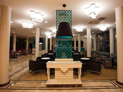 Großer Lobbyraum mit schwarzer Sofagruppe, braunem Tisch, Säulen und gemusterten Wänden.