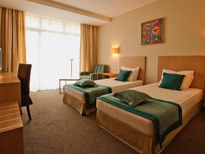 Gemütliches Hotelzimmer mit zwei Einzelbetten, Holzmöbeln und großem Fenster mit Vorhängen.