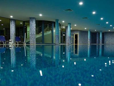 Großes Hallenbad mit blauen Fliesen, Wasserreflexionen und großen Fenstern bei Nacht.