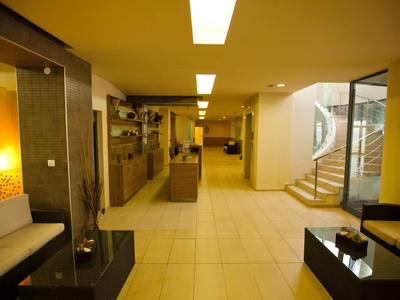 Moderner, heller Empfangsbereich mit Sitzmöbeln, Rezeption und Treppe, warme Beleuchtung, Fliesenboden.