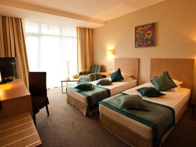 Hotelzimmer mit zwei Einzelbetten, Teppichboden, warmem Licht und hellen Vorhängen.