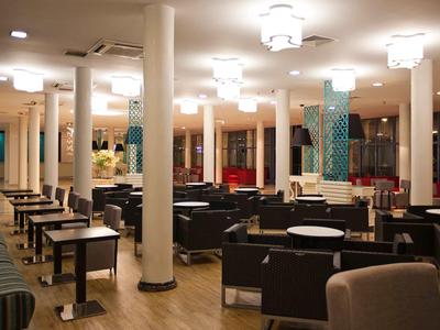 Area lounge hotel modernamente arredata con tavoli, sedie e illuminazione.