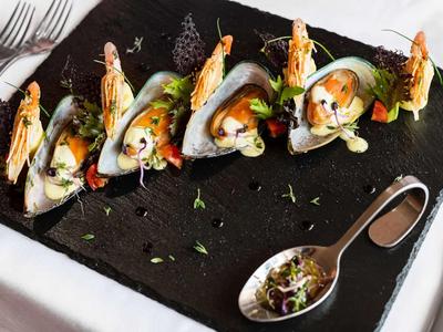 Elegante presentazione di ostriche su un vassoio nero con gamberi e erbe.
