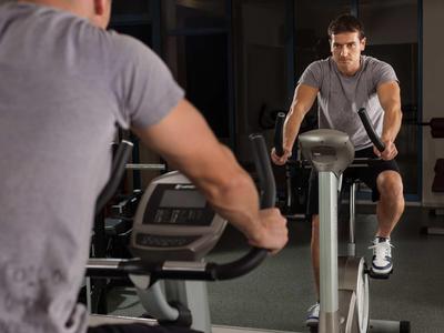 Uomo che si allena su una cyclette in palestra con specchi e pesi.