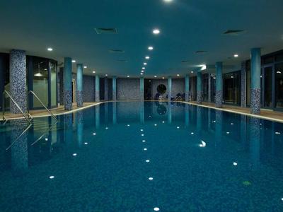 Elegante piscina coperta con piastrelle blu, lettini e grandi finestre con vista esterna.