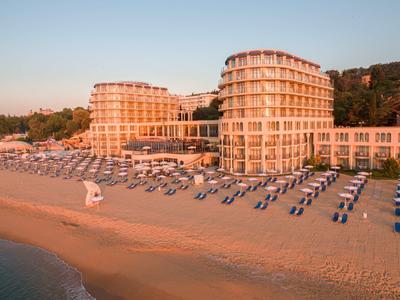 Großes Hotel mit runden Türmen am Strand, Sonnenschirme und Liegen in Reihen auf Sand.