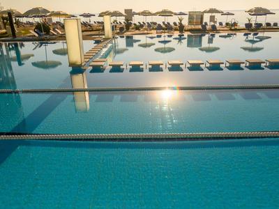Grande piscina all'aperto di un hotel con lettini e ombrelloni al tramonto.