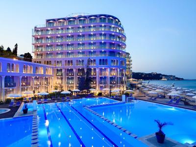 Hotel moderno con piscina illuminata vicino al mare al tramonto.