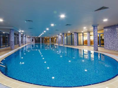 Ein ruhiges Hallenbad mit blauem Wasser, weißen Säulen und warmem Licht an der Decke.