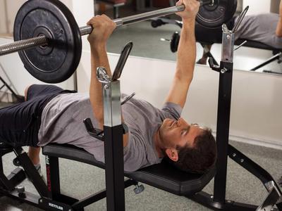 Uomo che fa panca piana con bilanciere in palestra.