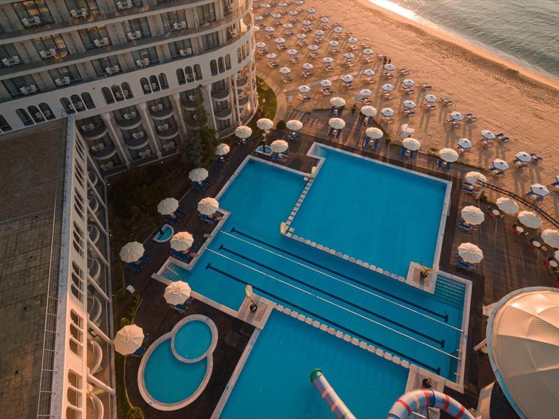Hotelpool mit mehreren Schwimmbecken und Sonnenschirmen am Strand bei Sonnenuntergang.