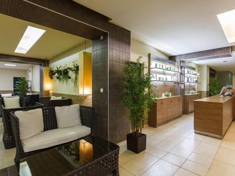 Moderne, helle Empfangshalle mit Sitzbereich, Pflanzen und Holztheke, weiße Kissen und Deckenlicht.