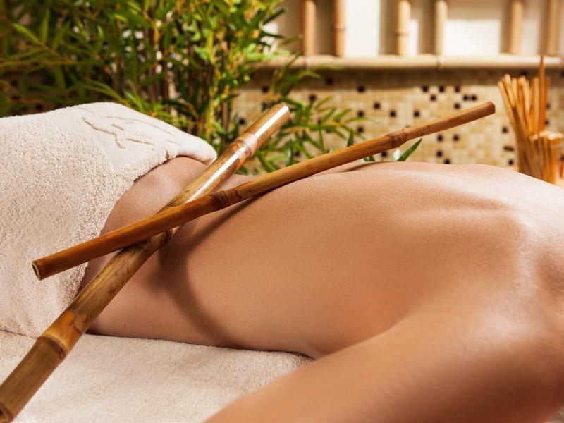 Eine Person liegt entspannt mit nacktem Rücken, zwei Bambusstöcke liegen darauf, entspannte Stimmung.