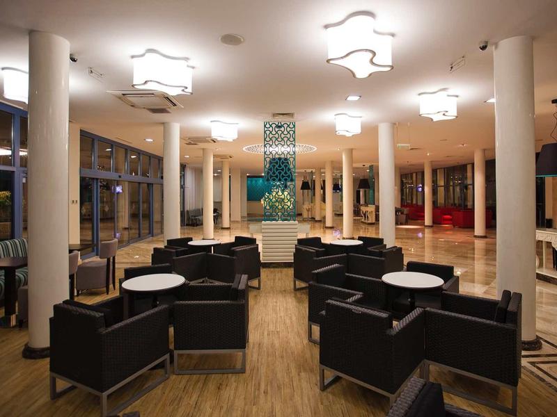 Moderner Aufenthaltsraum mit schwarzen Sitzgruppen, runden weißen Tischen und großen Fenstern bei Nacht.