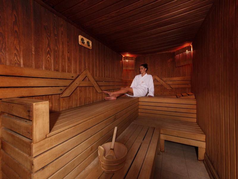 Holzsauna mit Sitzbänken, Holzlöffel und einem Mann in weißem Hemd.