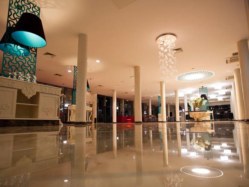 Großer Innenraum mit glänzendem Marmorboden, blauen Hängelampen und Säulen unter warmem Licht.