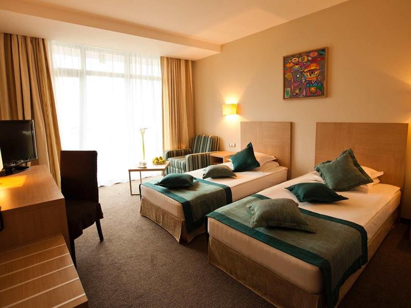 Hotelzimmer mit zwei Einzelbetten, Teppichboden, warmem Licht und hellen Vorhängen.