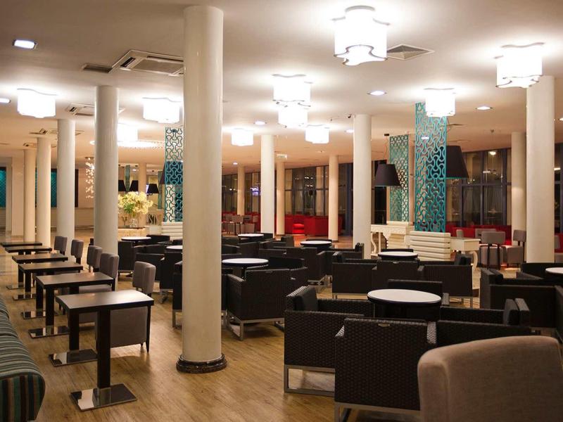 Großer, moderner Speisesaal mit schwarzen Sitzgruppen, weißem Säulendesign und warmem Licht.