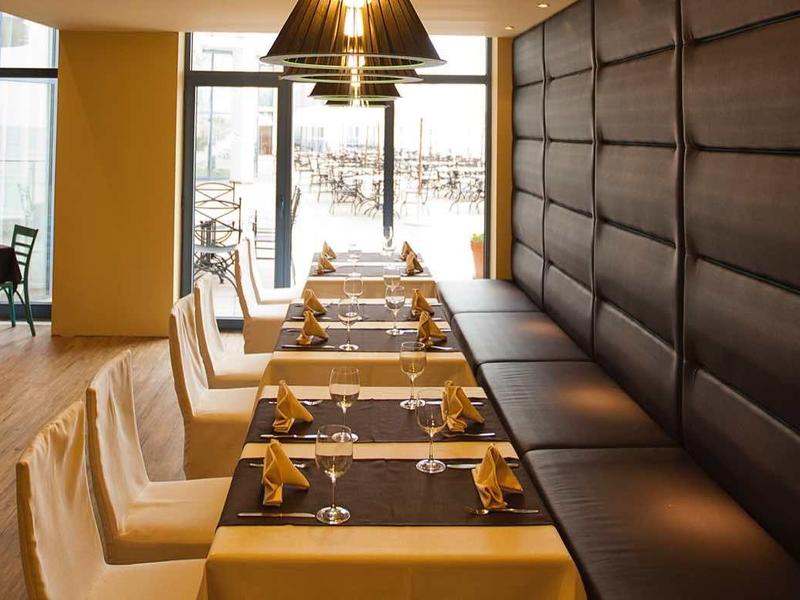 Modernes Restaurant mit braunen Lederbänken, cremefarbenen Stühlen und großen Fenstern.