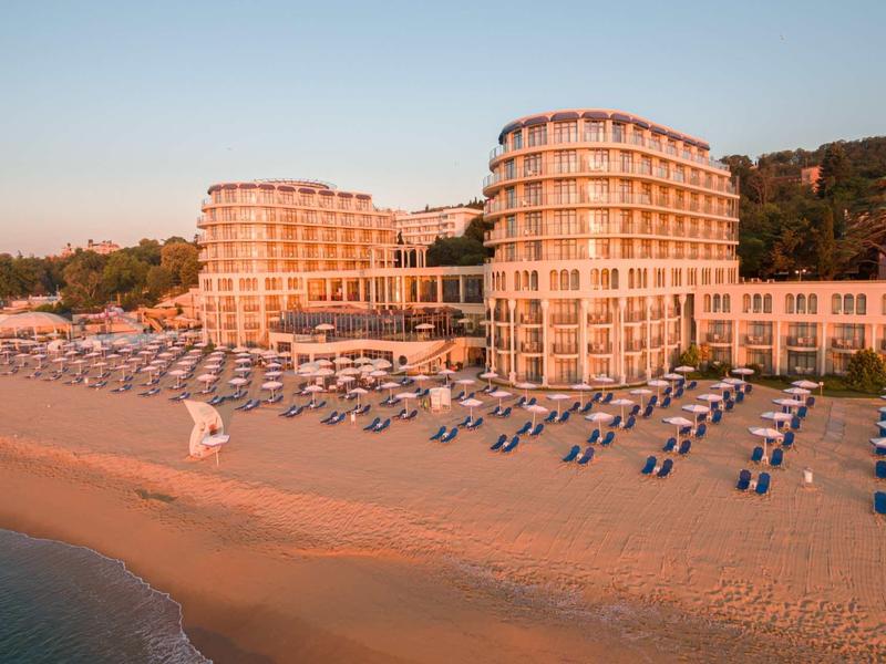 Großes Hotel mit runden Türmen am Strand, Sonnenschirme und Liegen in Reihen auf Sand.