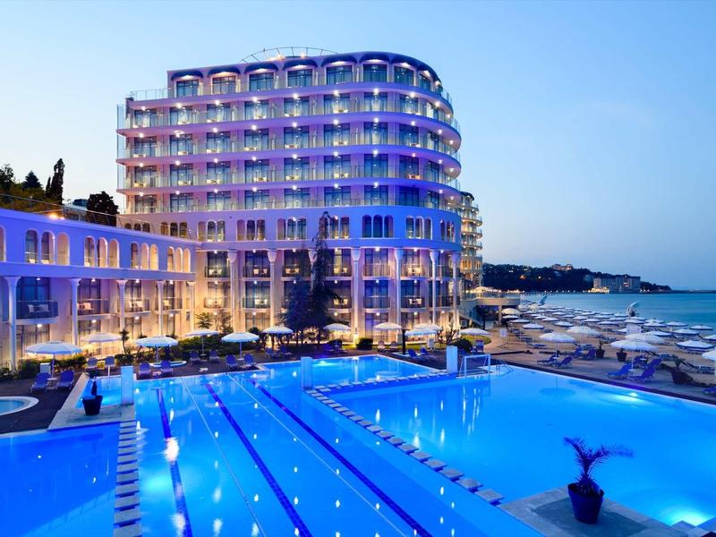 Modernes Hotel mit beleuchtetem Swimmingpool und Aussicht auf das blaue Meer bei Abenddämmerung.