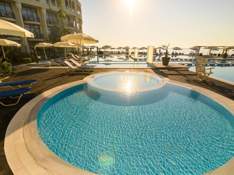 Runder blauer Pool mit klarem Wasser, umgeben von Liegestühlen und Sonnenschirmen bei Sonnenuntergang.