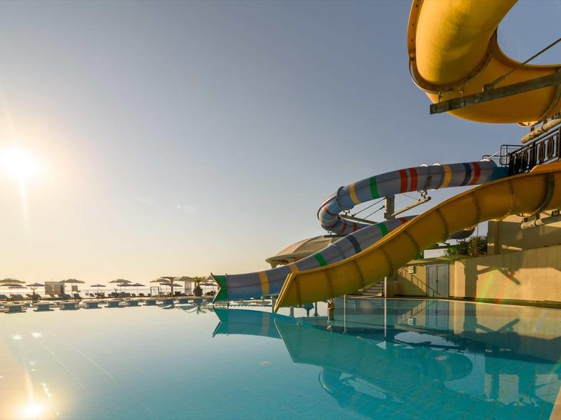 Wasserpark mit großen, bunten Wasserrutschen über klarem, blauem Pool bei Sonnenuntergang.