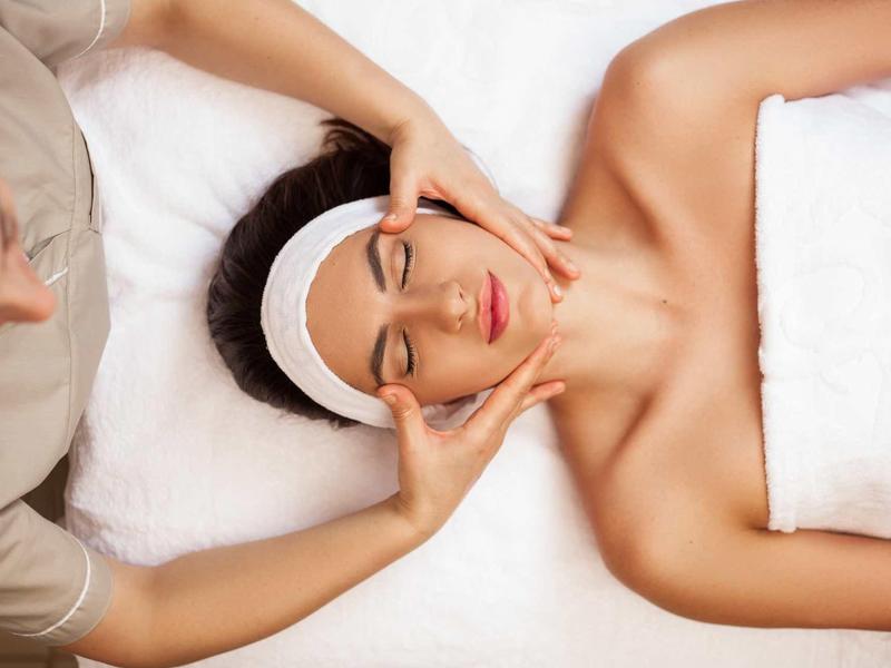 Eine Frau erhält im Spa eine entspannende Gesichtsmassage auf weißer Liege.