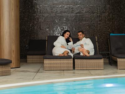 Pareja en albornoces relajándose en muebles junto a una piscina.