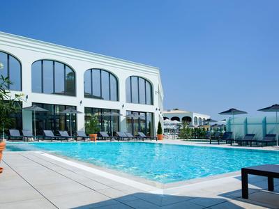 Piscina moderna dell'hotel con lettini e ombrelloni sotto un cielo sereno.