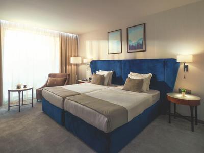 Habitación de hotel luminosa con dos camas individuales, tapicería azul y mobiliario moderno.