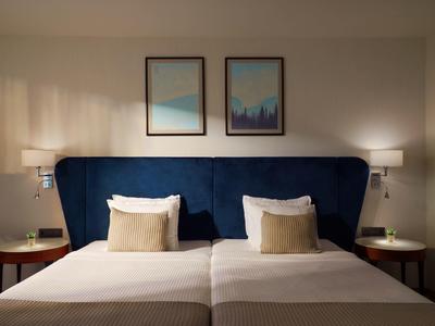 Cama doble con cabecero azul, cojines blancos y beige, dos mesas de noche con lámparas y luz cálida.