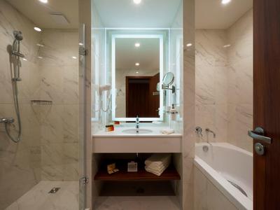 Baño moderno con ducha de cristal, lavabo blanco y bañera en tonos cálidos.