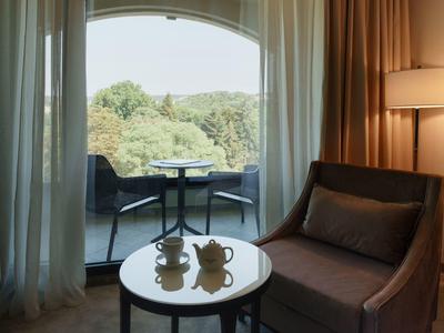 Área de descanso acogedora con ventana de cristal y vista a terraza y paisaje verde.