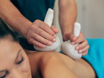 Mujer recibe un masaje con compresas de hierbas en la espalda en un spa.