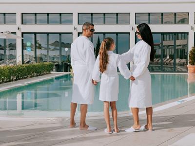 Familia con batas junto a la piscina de un hotel moderno en un día soleado.